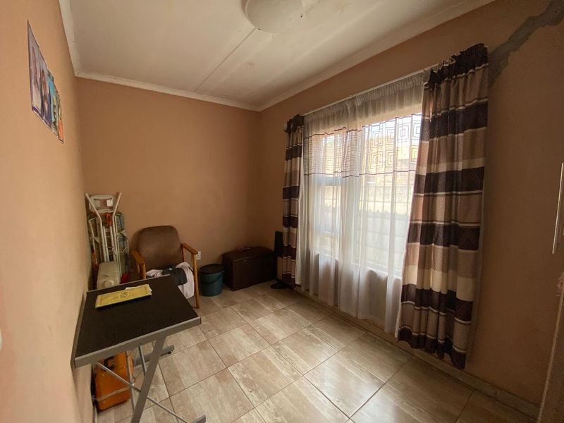 A bedroom featuring tiled flooring and a large window, currently showing signs of wear including a visible wall crack.