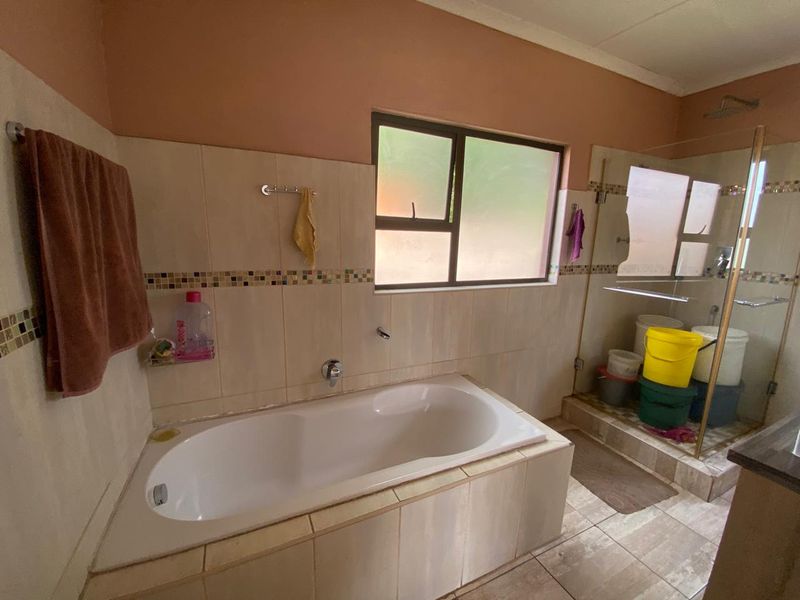 A functional bathroom featuring a built-in bathtub, a separate glass-enclosed shower, and neutral wall and floor tiling.