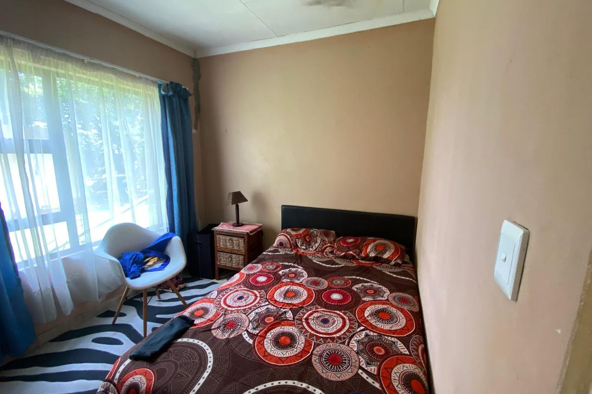 A bedroom featuring a large window and light switch, showing visible signs of ceiling water damage and wall cracking requiring maintenance.