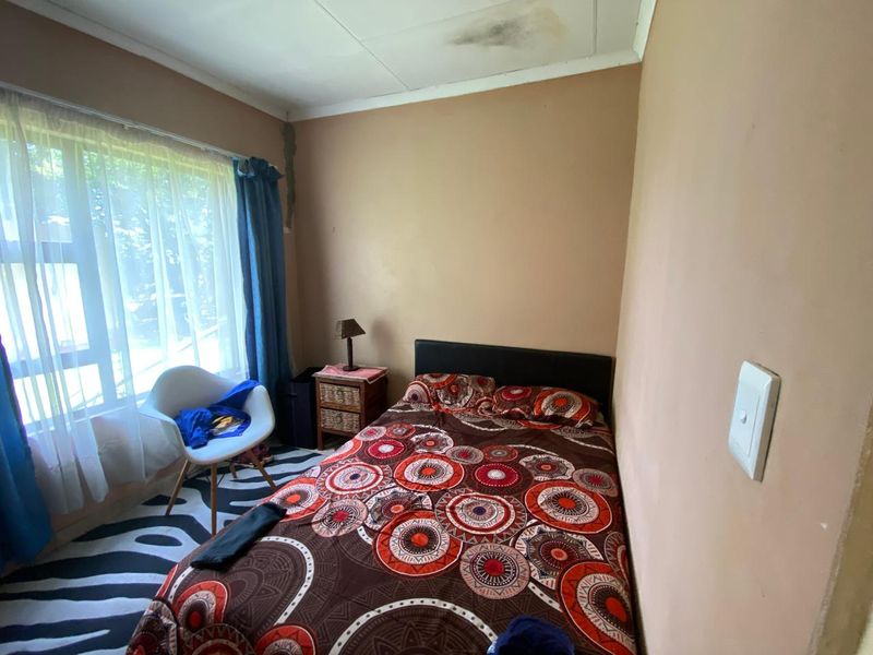 A bedroom featuring a large window and light switch, showing visible signs of ceiling water damage and wall cracking requiring maintenance.