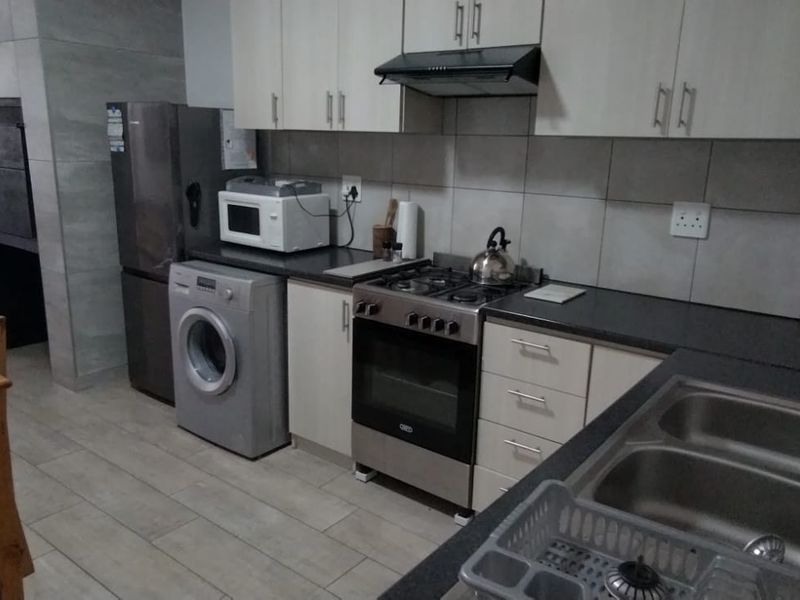 Open-plan kitchen featuring modern cabinetry, a gas stove with extractor, double basin sink, and tiled finishes, seamlessly flowing into the living area.