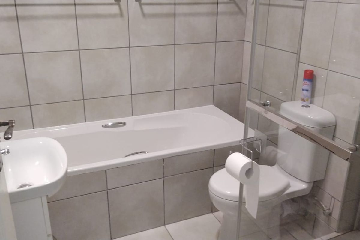 A clean, functional bathroom featuring a bathtub, a separate shower area with a glass screen, a toilet, and a wall-mounted washbasin with tiled finishes.