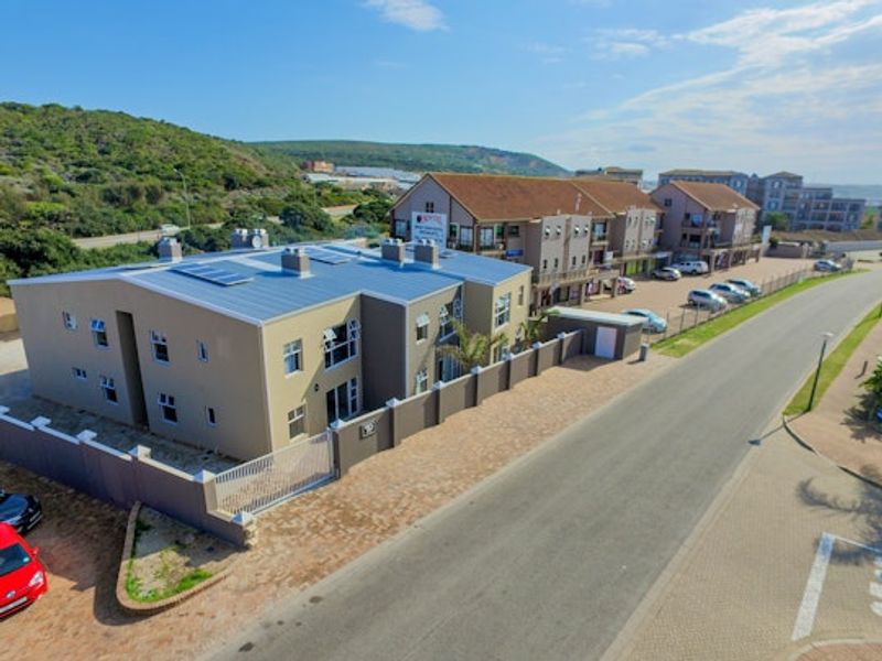 Aerial view of a modern apartment complex featuring a metal roof with solar panels, secure perimeter walling, and paved driveway access.
