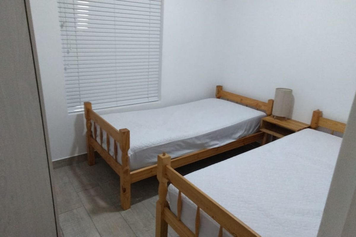 A functional bedroom featuring tiled flooring, a built-in cupboard, and venetian blinds, providing a clean and simple living space.