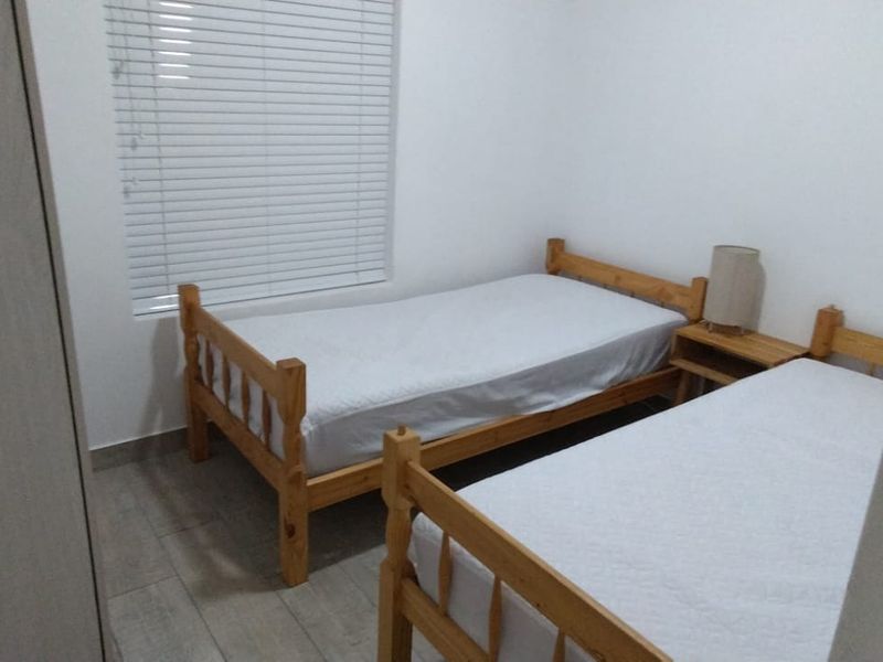 A functional bedroom featuring tiled flooring, a built-in cupboard, and venetian blinds, providing a clean and simple living space.