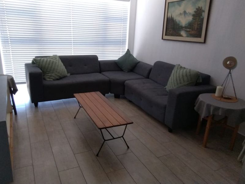 A comfortable living room featuring modern tiled flooring and large windows fitted with venetian blinds, providing ample natural light.
