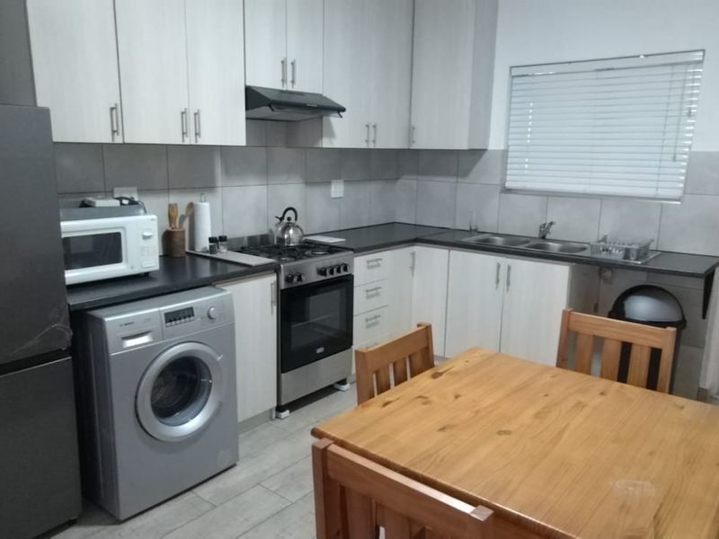 A functional kitchen featuring light-toned cabinetry, dark laminate countertops, a gas stove with extractor fan, and tiled finishes throughout.