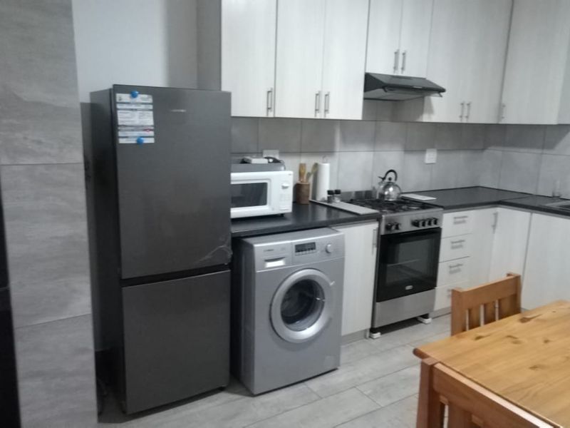 A functional kitchen featuring light-toned cabinetry, a tiled backsplash, built-in oven and hob, and a double sink with tiled flooring throughout.