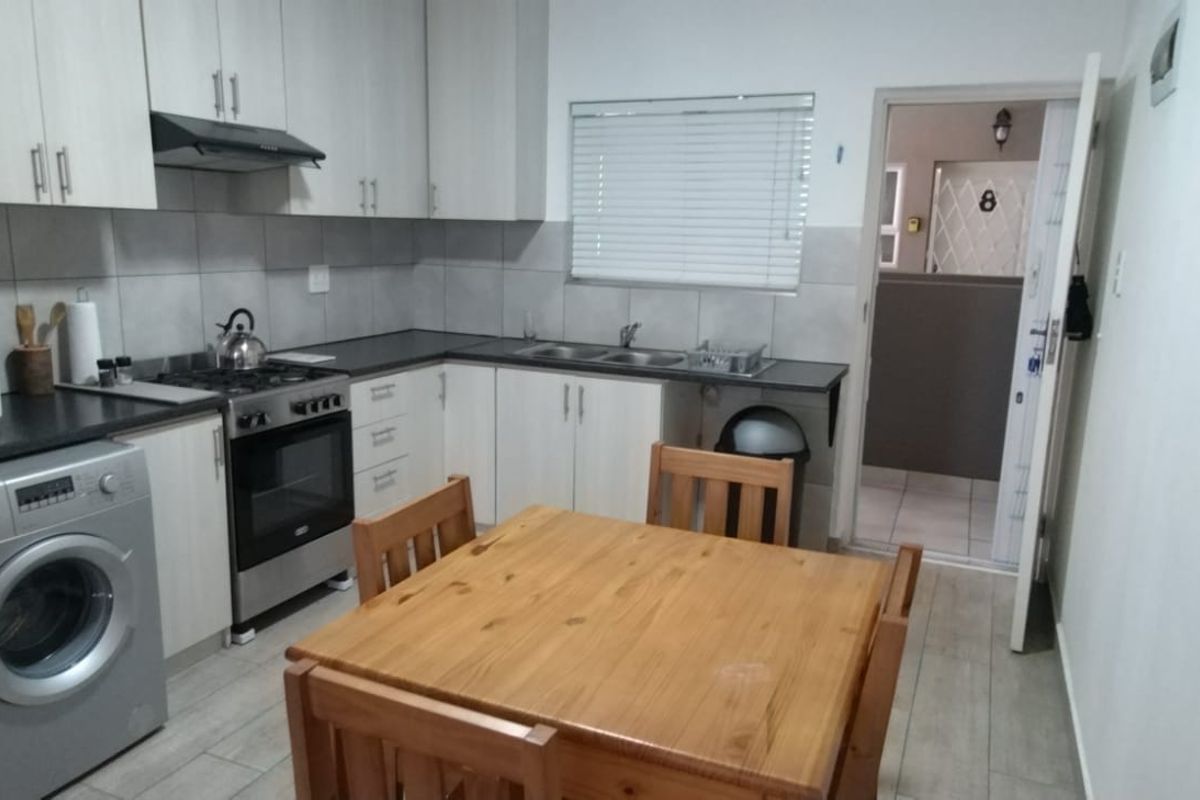 A functional kitchen featuring light-toned cabinetry, a gas hob with extractor fan, double sink, and tiled backsplash, with direct access to an adjacent hallway.
