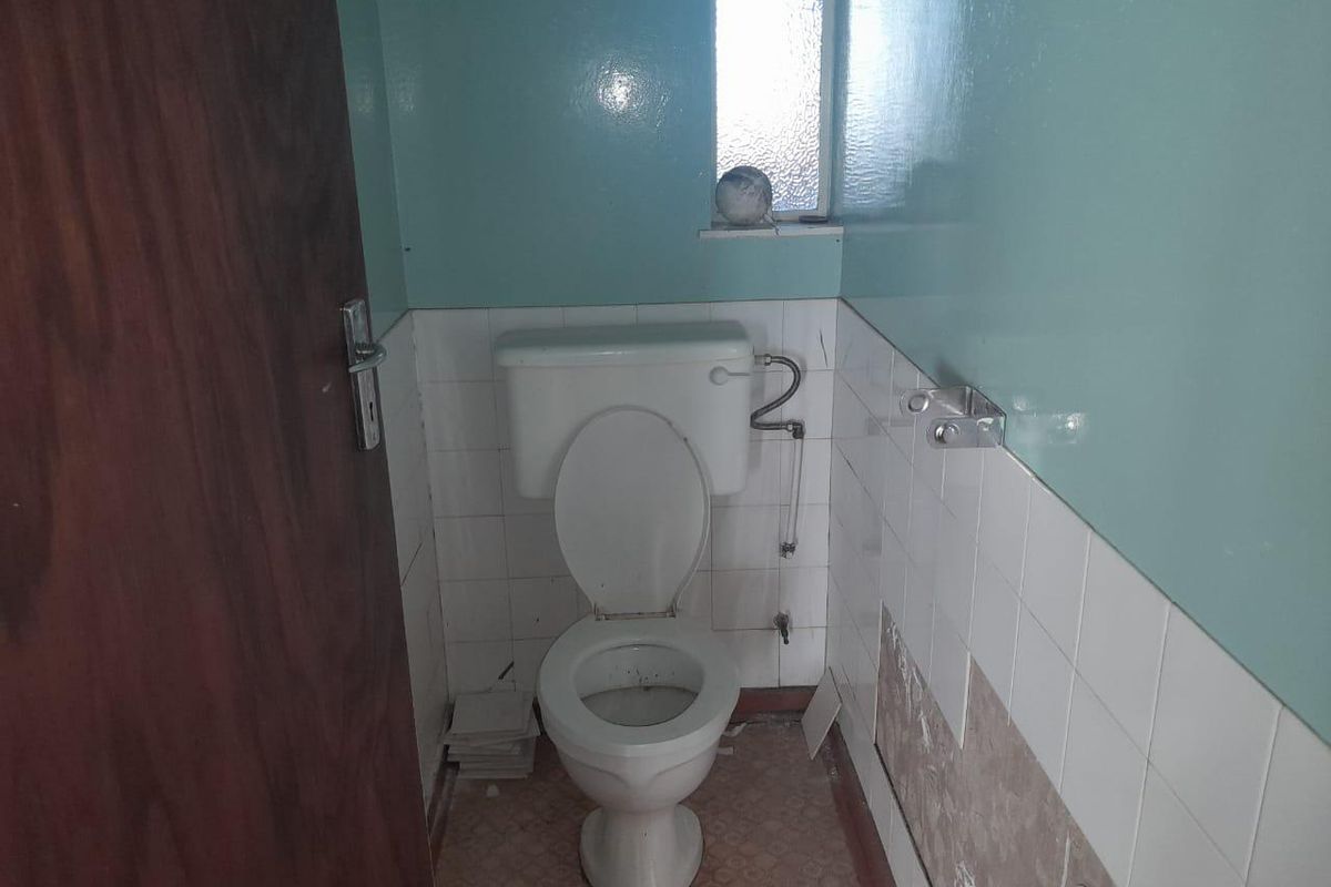 A small, dated bathroom featuring a standard toilet, partially tiled walls, and worn flooring, requiring renovation and cosmetic updates.