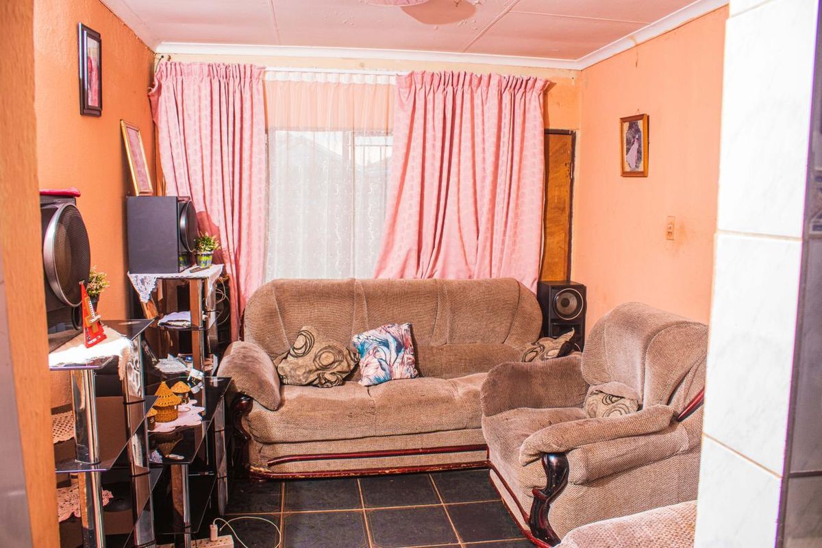 A compact living room featuring dark floor tiles and a window with curtains, offering a functional space for relaxation.