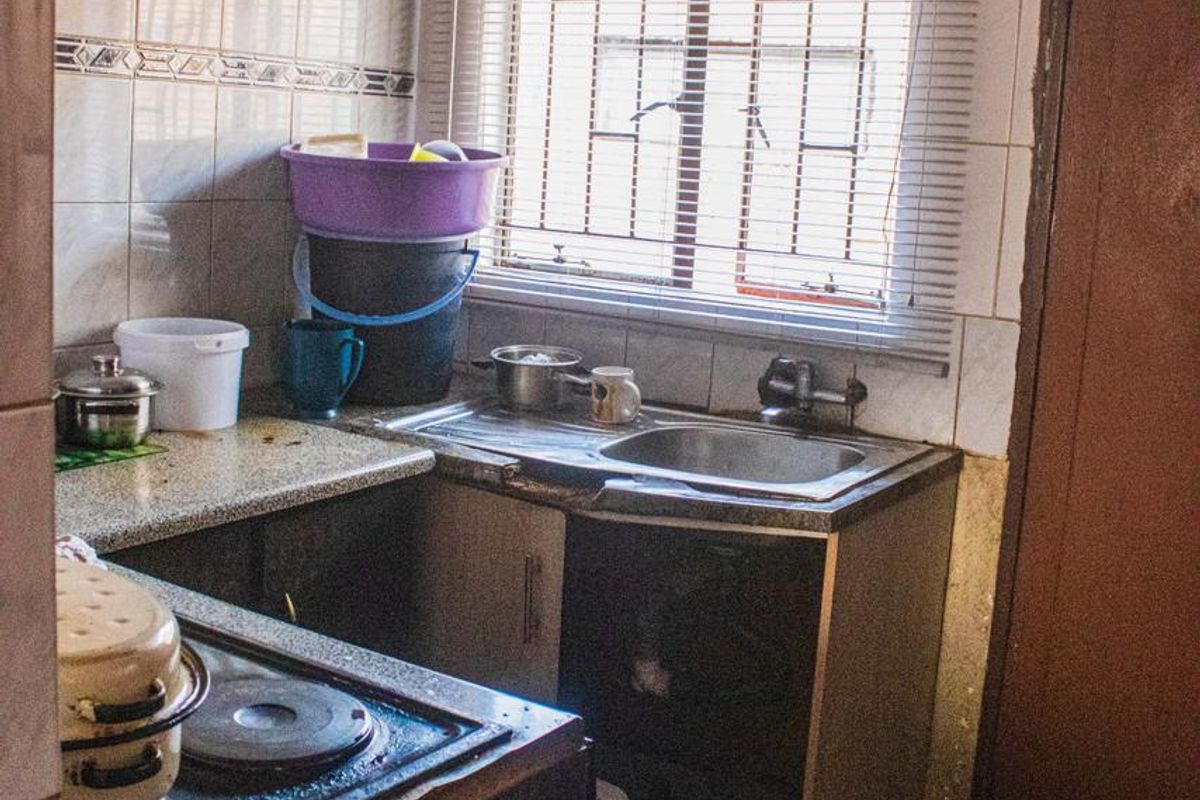 A compact kitchen featuring a built-in stove, extractor fan, stainless steel sink, and tiled finishes, requiring significant renovation and maintenance.