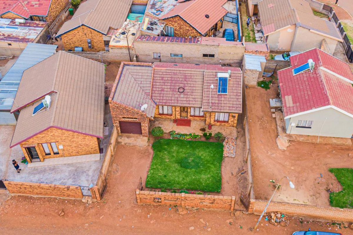 Aerial view of a residential property featuring a brick facade, tiled roof, solar water heating system, and a front garden with a lawn.