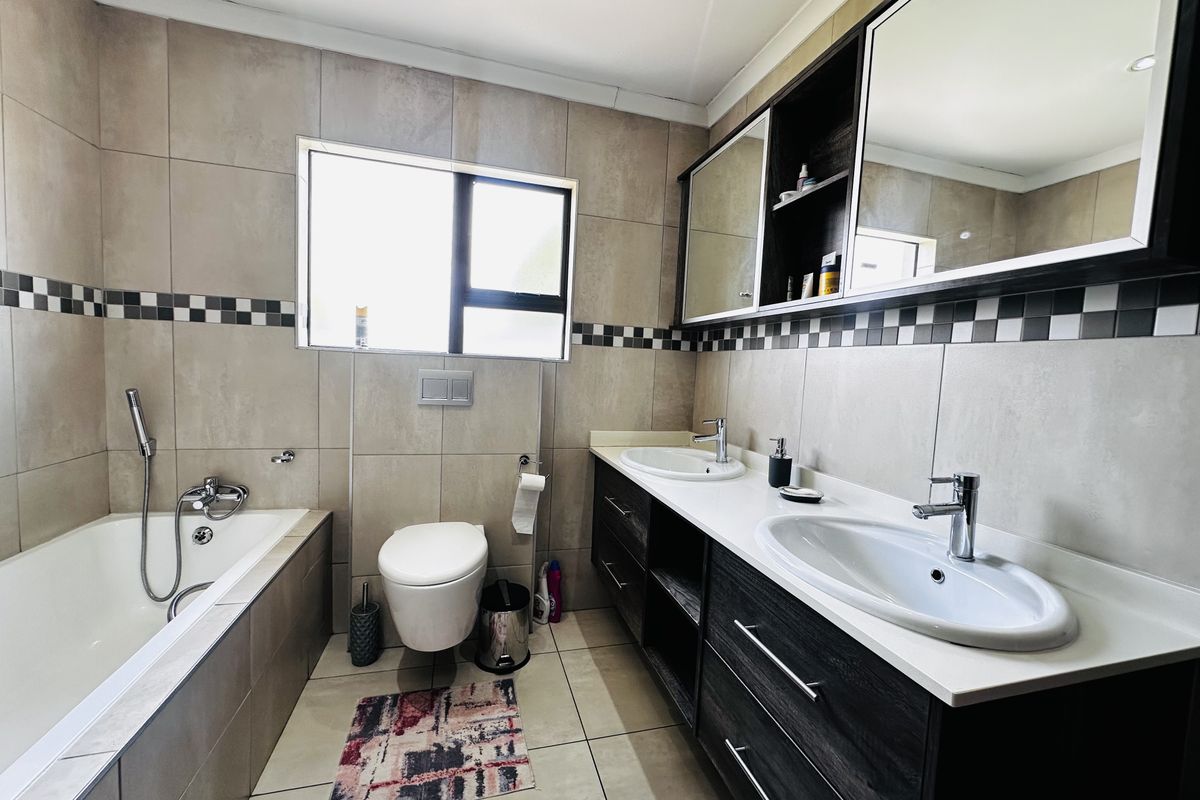 Modern bathroom featuring a double vanity with dark cabinetry, wall-mounted toilet, and a tiled bathtub area with a handheld shower mixer.