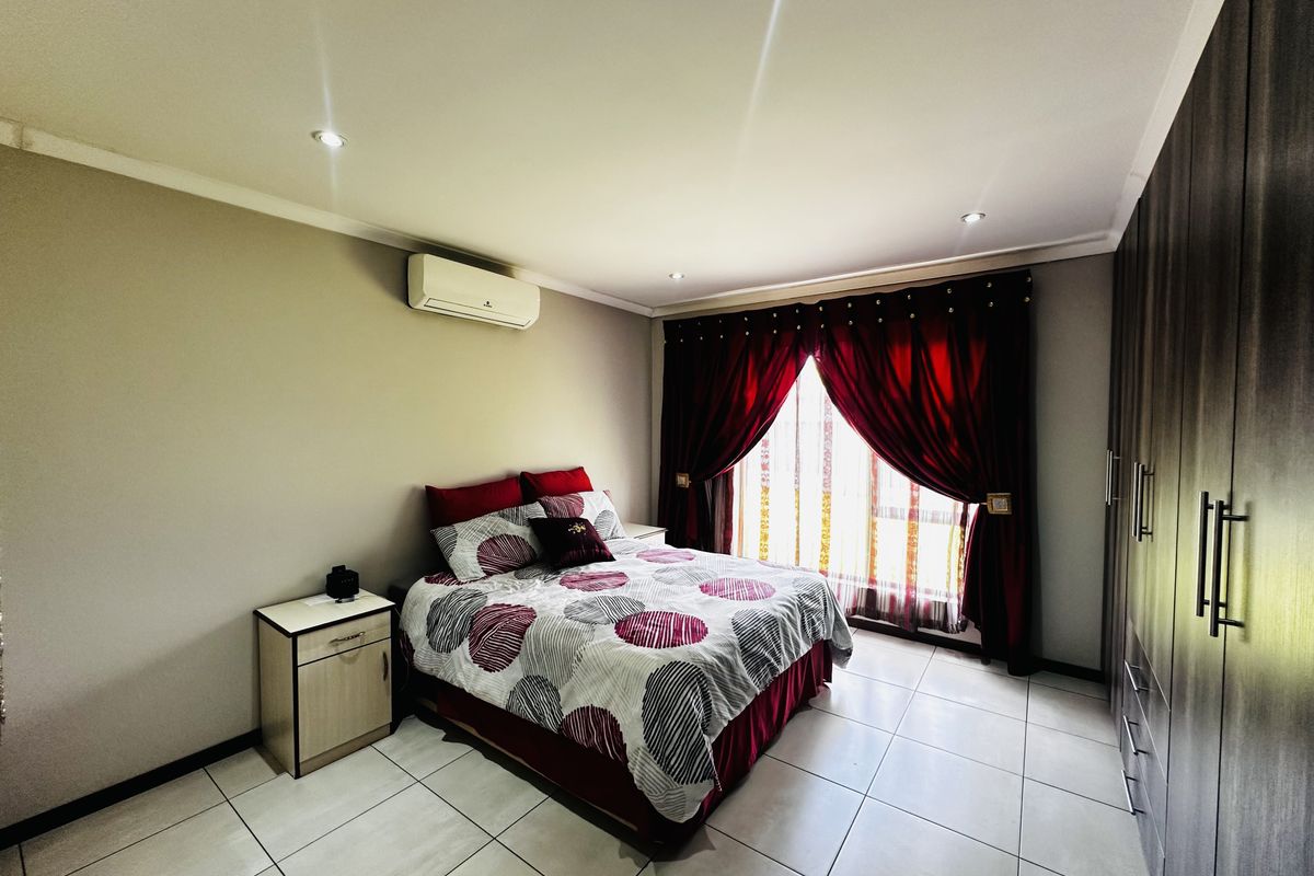 A well-maintained bedroom featuring tiled flooring, built-in cupboards, recessed downlighting, and a wall-mounted air conditioning unit.