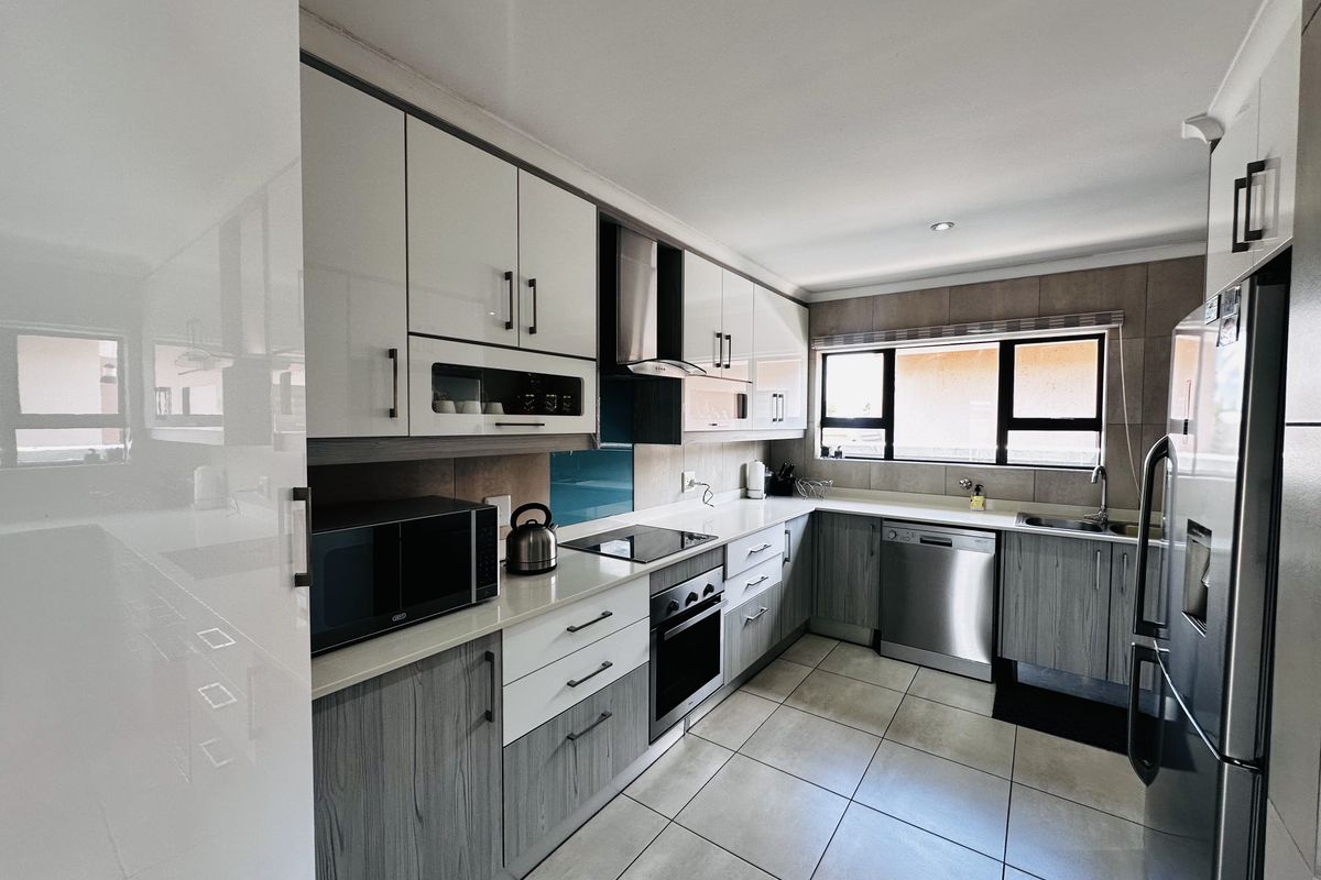 Modern kitchen featuring two-tone cabinetry, stone countertops, integrated appliances, electric hob, and tiled flooring with a functional layout.