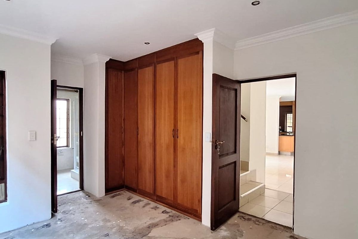 An empty bedroom featuring built-in wooden cupboards, recessed downlights, and cornicing, requiring flooring repairs to complete the space.