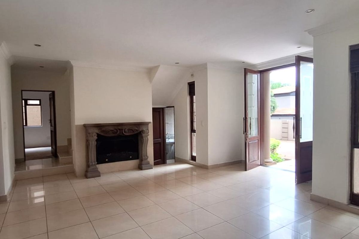 Spacious living room featuring tiled flooring, a stone fireplace, and double doors opening to the exterior, providing a bright and open atmosphere.