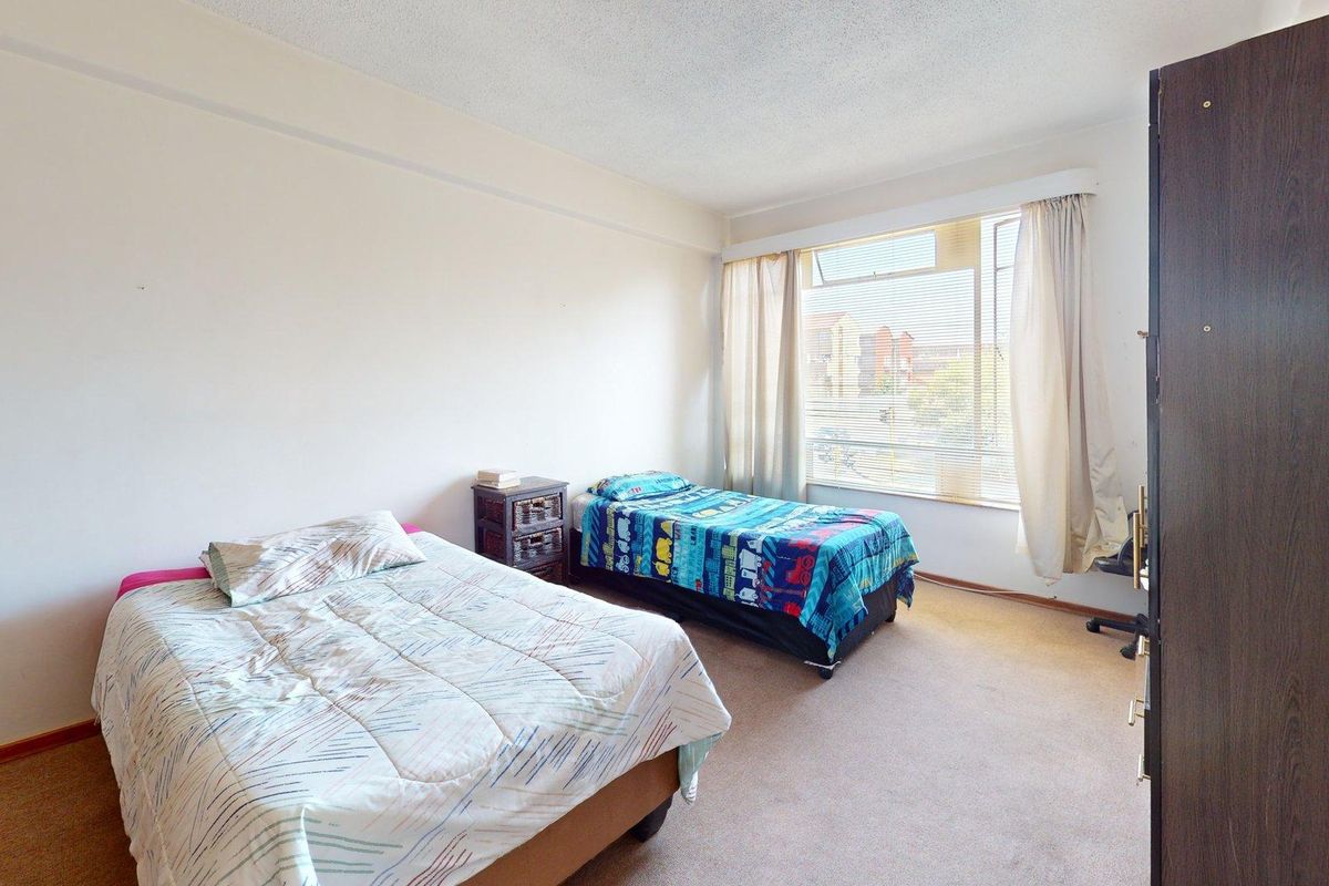 A spacious bedroom featuring carpeted flooring and a large window allowing natural light, providing a functional space ready for modernization.