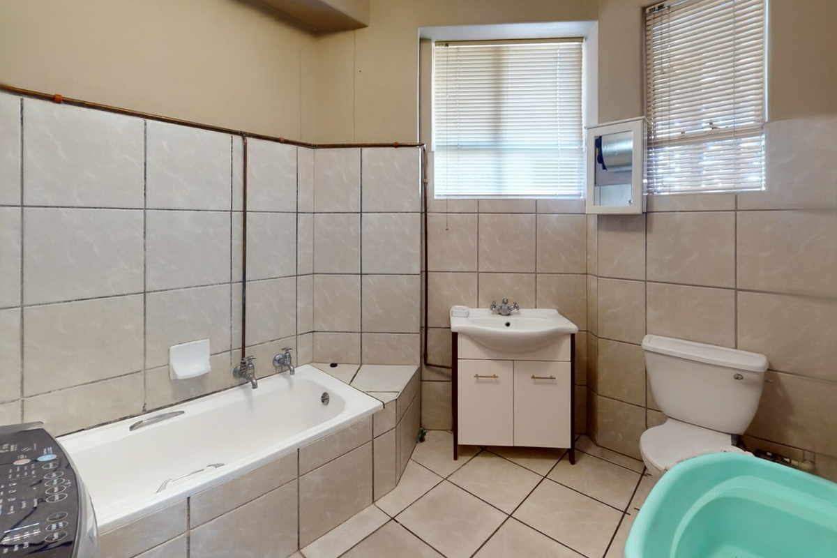 A functional bathroom featuring a bathtub, vanity cabinet with basin, and toilet, finished with neutral wall and floor tiles.