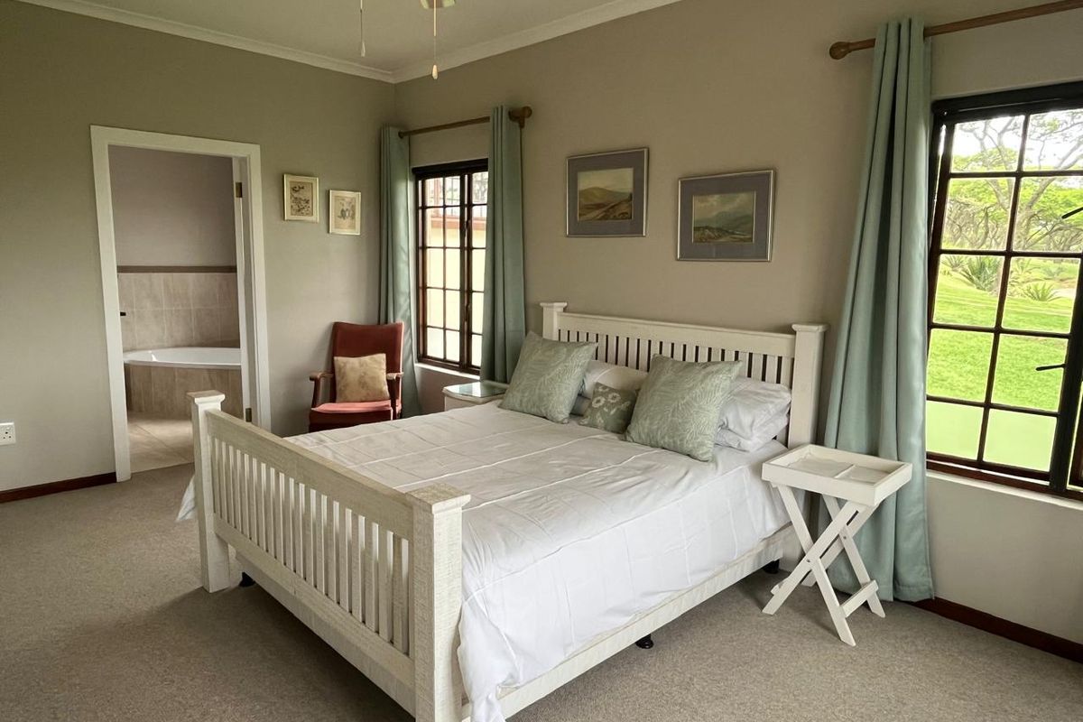 Spacious bedroom featuring neutral walls, carpeted flooring, lattice windows with garden views, and an adjoining en-suite bathroom.