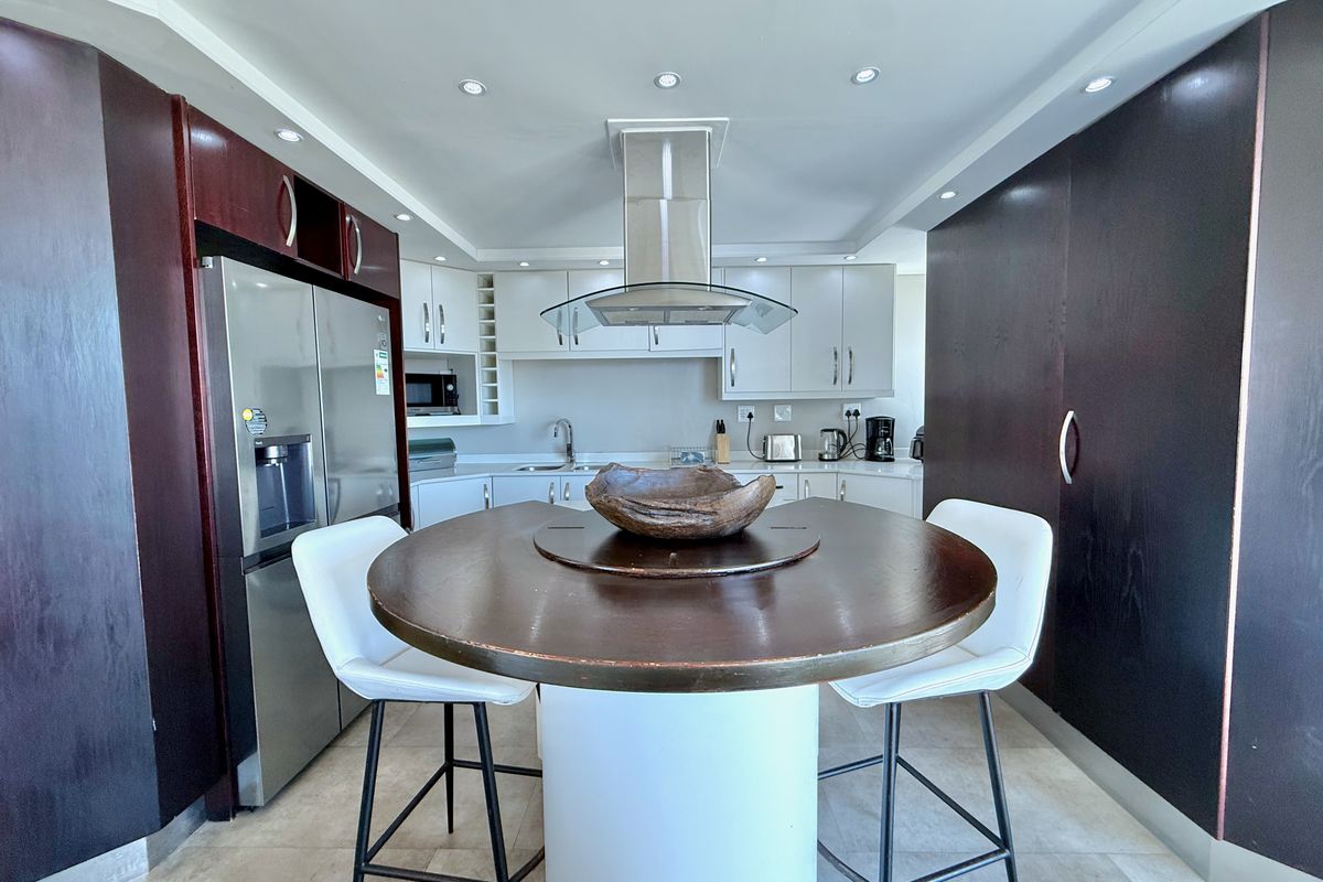 Modern kitchen featuring dark wood cabinetry, white upper cabinets, a central island with breakfast seating, and a stainless steel extractor fan.