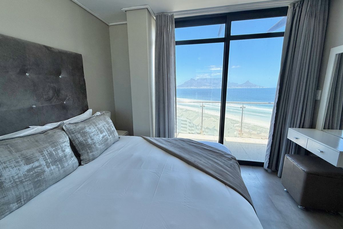 A well-appointed bedroom featuring floor-to-ceiling windows that offer expansive ocean and mountain views, providing a bright and airy atmosphere.