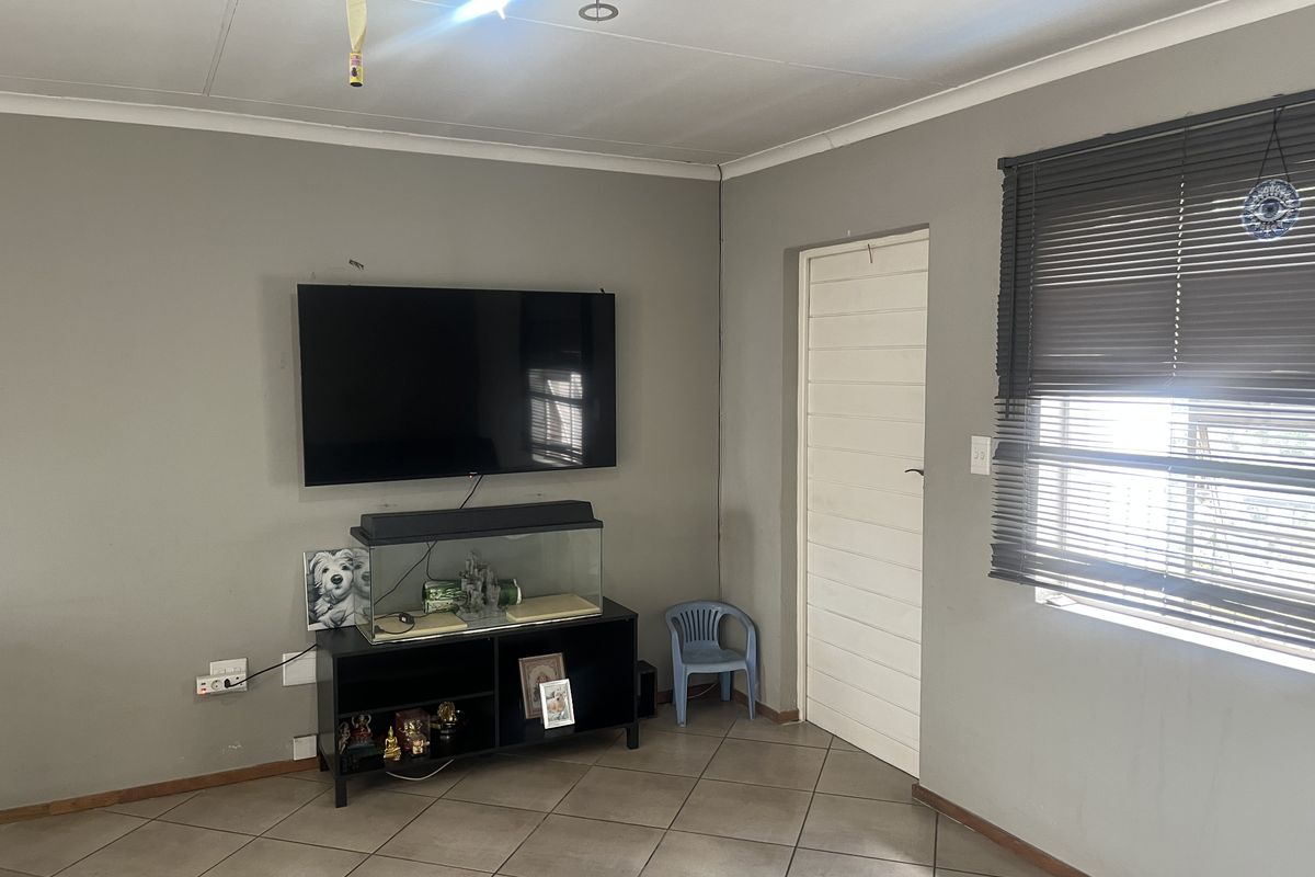 A living room featuring neutral grey walls, ceramic tiled flooring, and venetian blinds, providing a functional space ready for cosmetic updates.