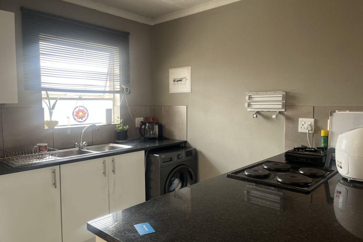 Functional kitchen featuring dark granite countertops, white cabinetry, tiled splashback, and a built-in electric hob with integrated sink area.