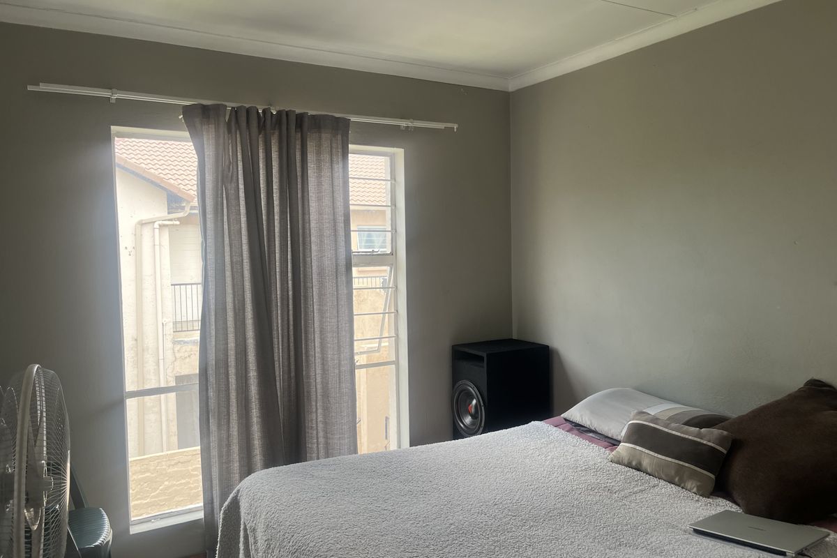 A standard bedroom featuring tiled flooring, a window with security bars, and neutral wall paint.