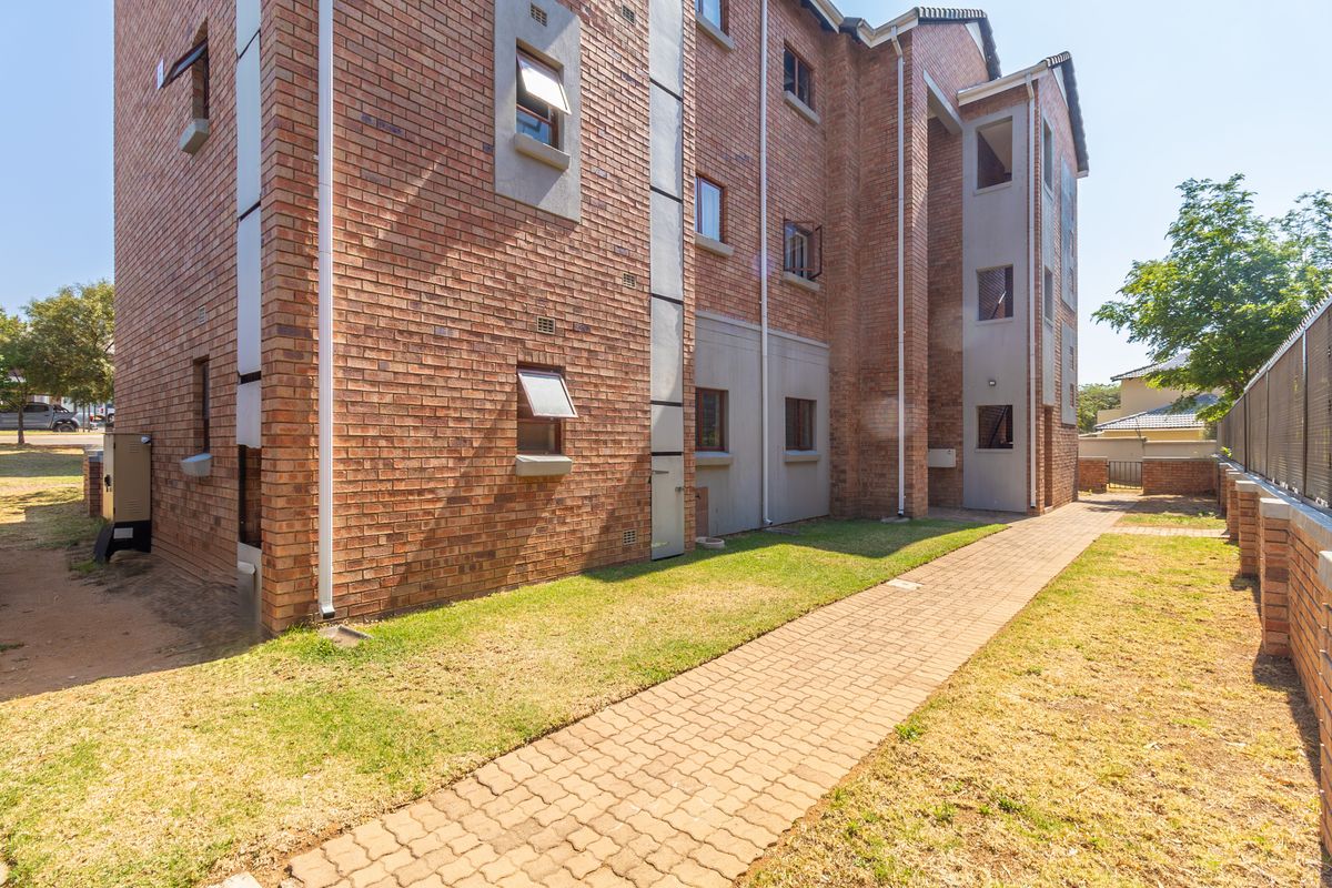 Exterior view of the apartment building featuring a face brick facade, paved walkway, and established lawn area.