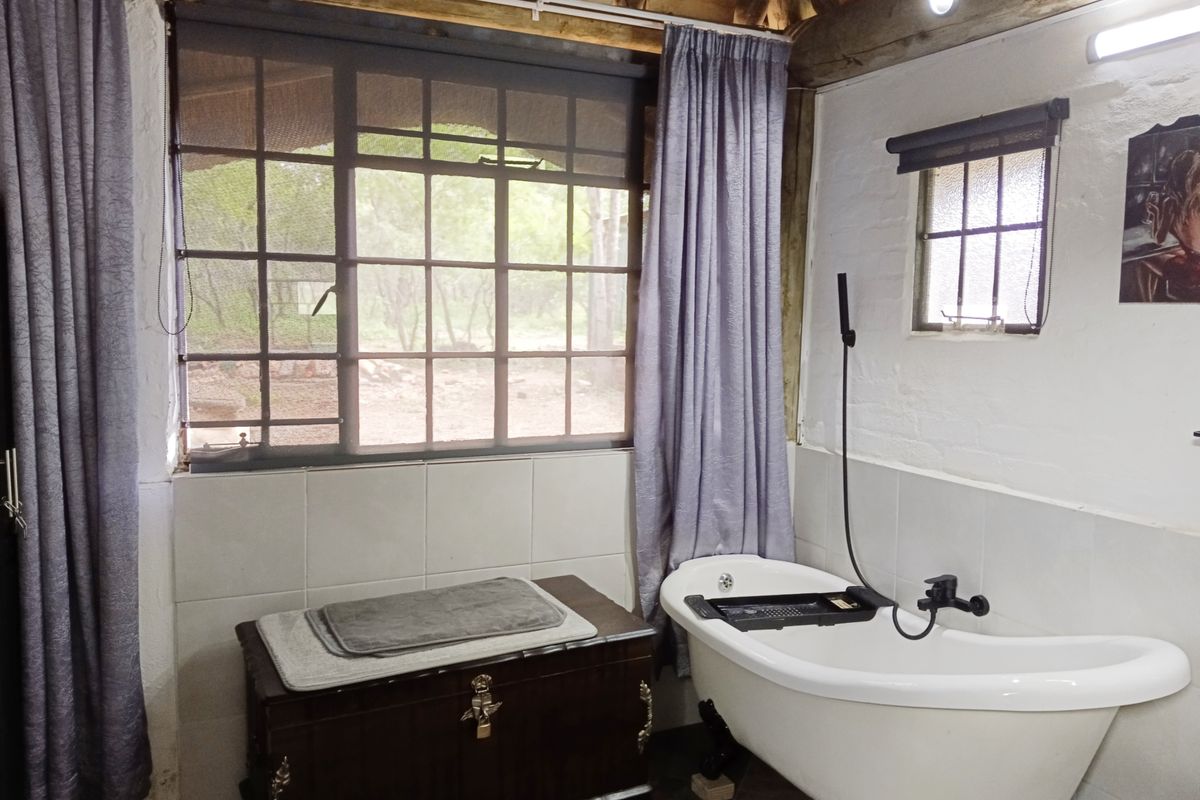 A rustic-style bathroom featuring a freestanding bathtub, exposed timber ceiling beams, and large windows overlooking the natural surroundings.