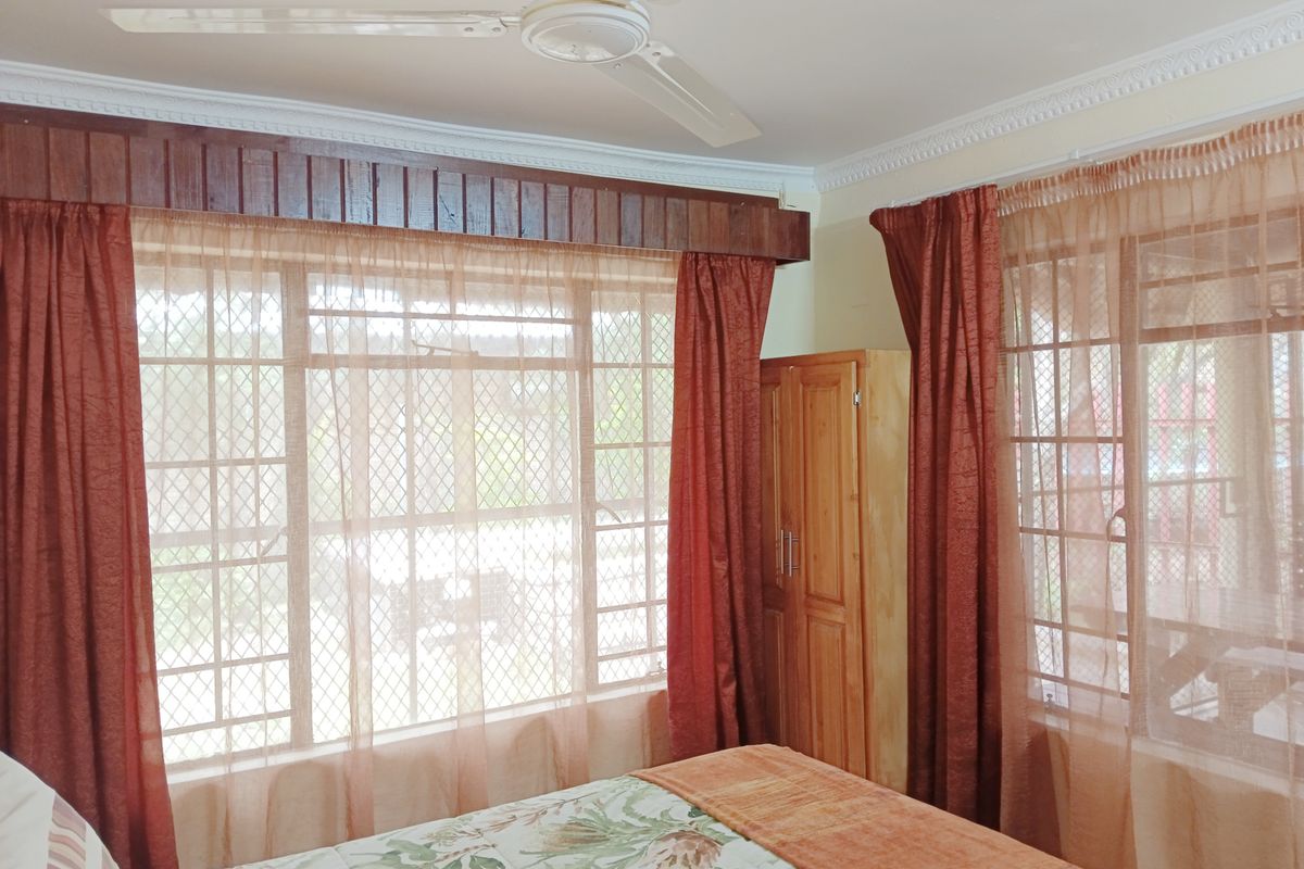A bedroom featuring a ceiling fan, built-in timber wardrobe, and large windows fitted with security bars and decorative timber pelmets.