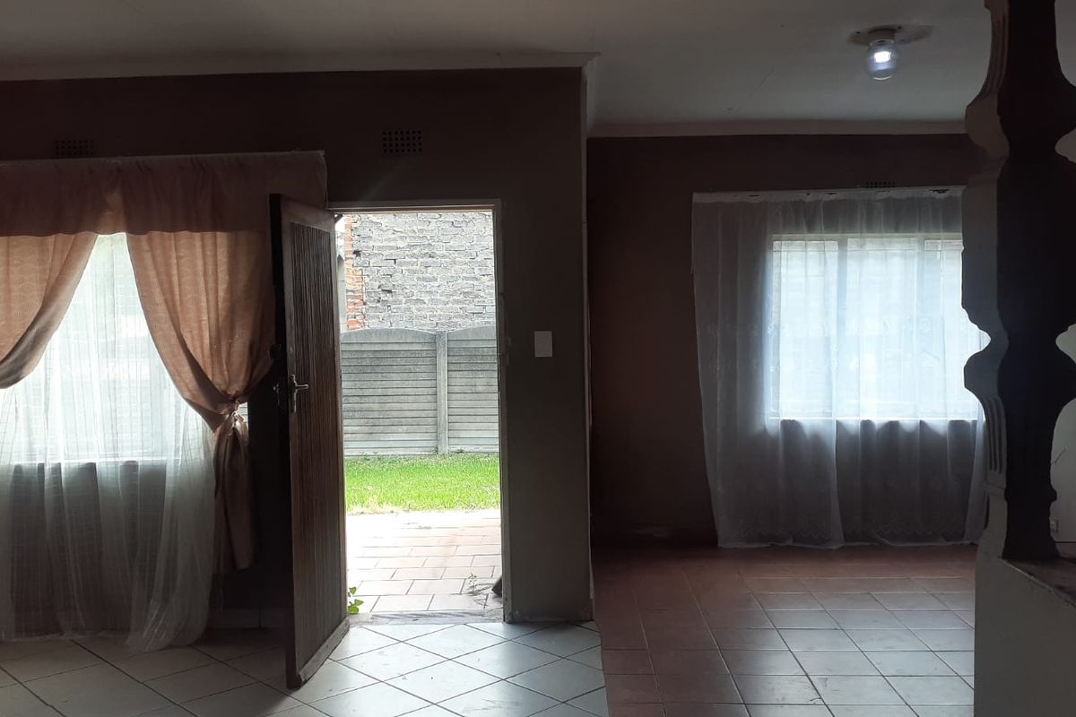 An empty living room featuring tiled flooring, natural light from windows, and direct access to the rear exterior area.