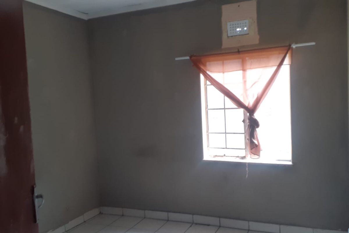 An empty bedroom featuring tiled flooring and a window with security bars, requiring cosmetic updates to improve its overall appeal.