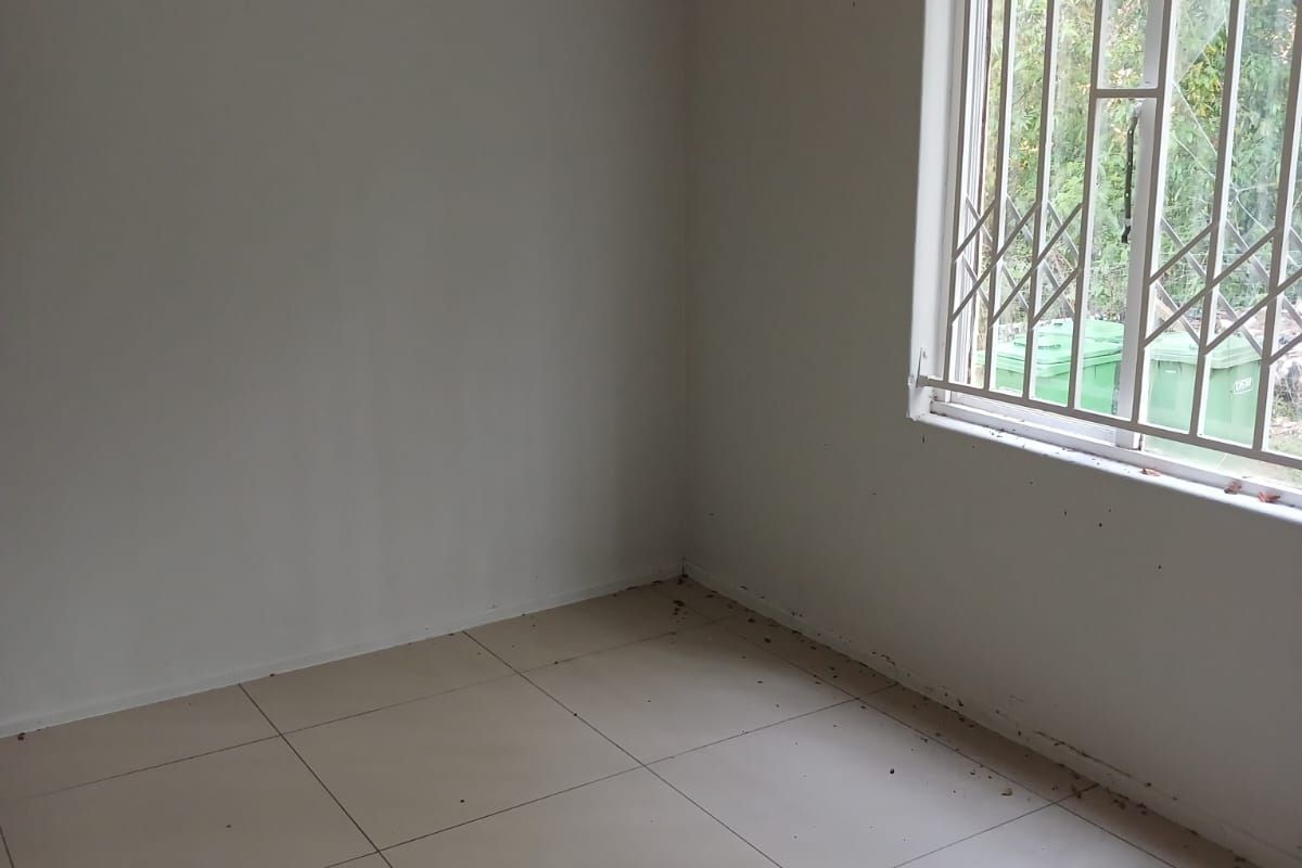 An empty bedroom featuring tiled flooring and a window with a security gate. The room requires cleaning and minor repairs to the window pane.