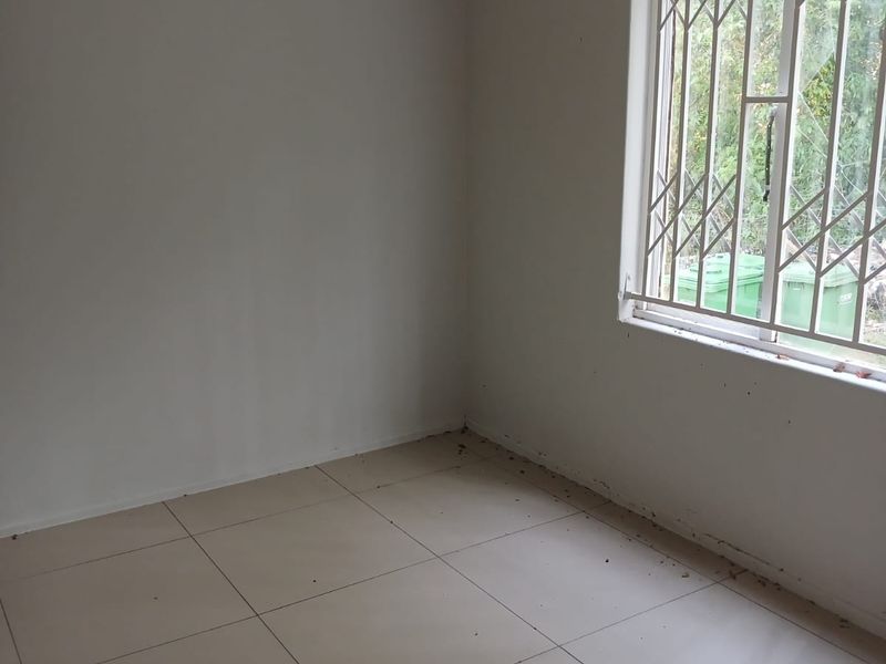 An empty bedroom featuring tiled flooring and a window with a security gate. The room requires cleaning and minor repairs to the window pane.