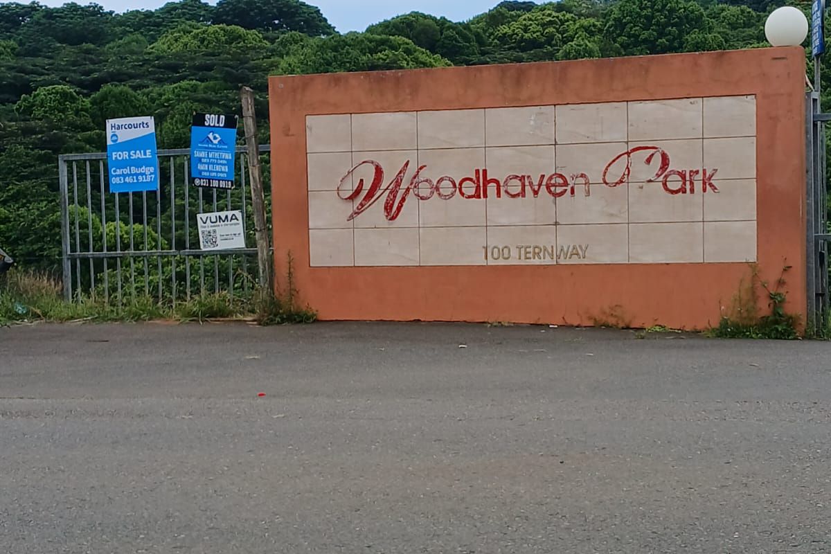 Entrance view of Woodhaven Park featuring a boundary wall with signage and a security gate.