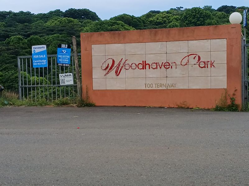 Entrance view of Woodhaven Park featuring a boundary wall with signage and a security gate.