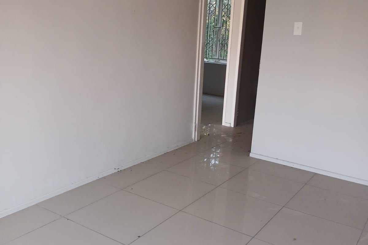 An empty, neutral-toned living area featuring ceramic floor tiles and a doorway leading to an adjacent room.