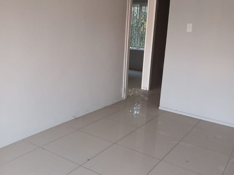 An empty, neutral-toned living area featuring ceramic floor tiles and a doorway leading to an adjacent room.