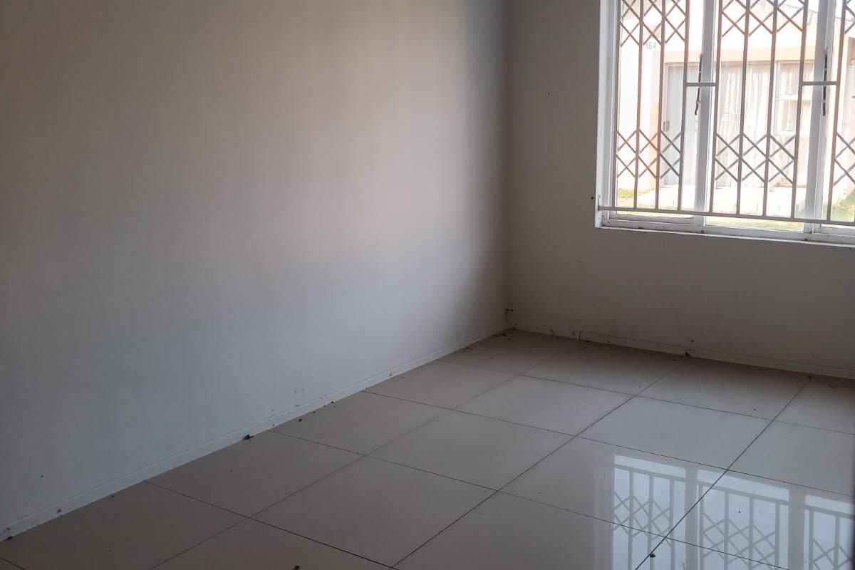 An empty bedroom featuring neutral tiled flooring and a window fitted with a security gate.