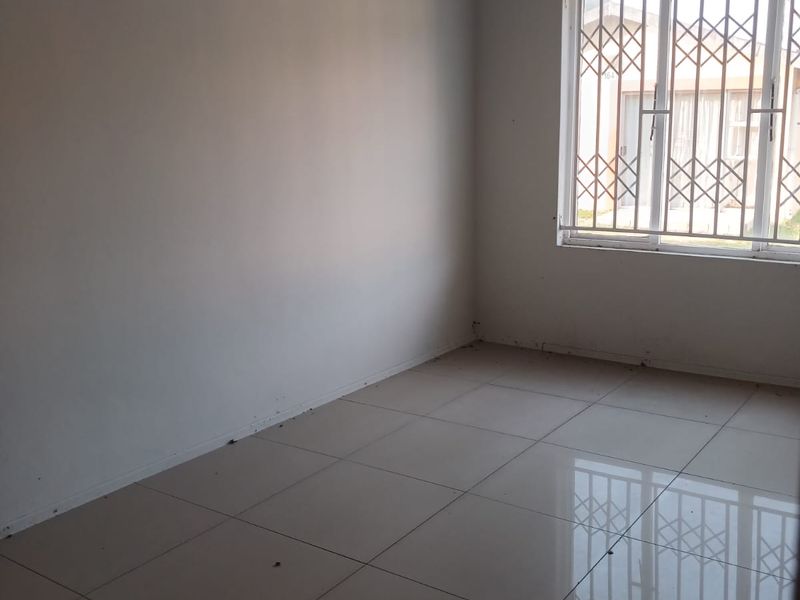 An empty bedroom featuring neutral tiled flooring and a window fitted with a security gate.