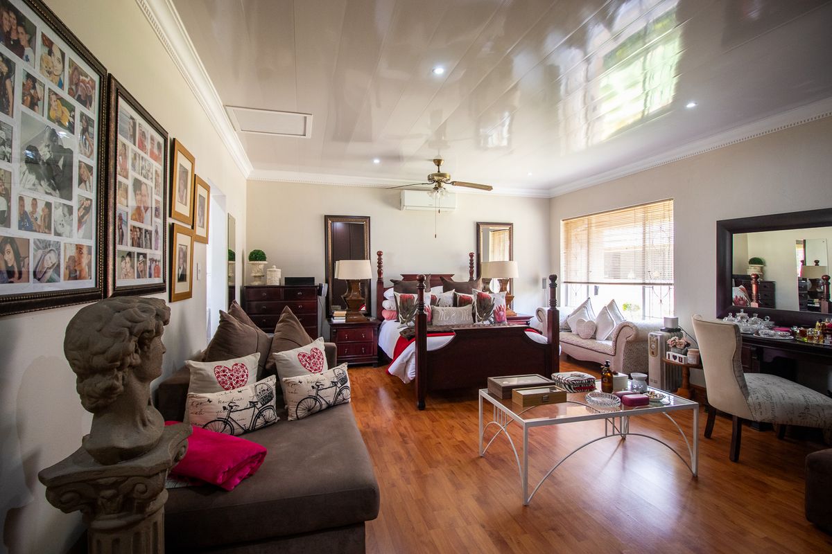 Spacious bedroom featuring laminate flooring, a ceiling fan, and a wall-mounted air conditioning unit, offering a comfortable and well-maintained living space.