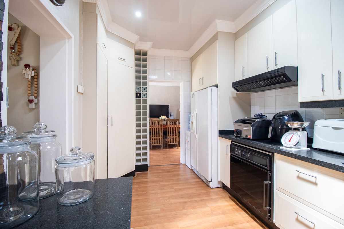 A functional kitchen featuring white cabinetry, black granite countertops, built-in oven, extractor fan, and integrated wine storage, with laminate flooring and coved cornicing.