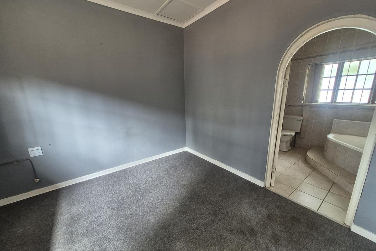 An empty bedroom featuring grey carpeting and an arched doorway leading into an en-suite bathroom with tiled finishes.