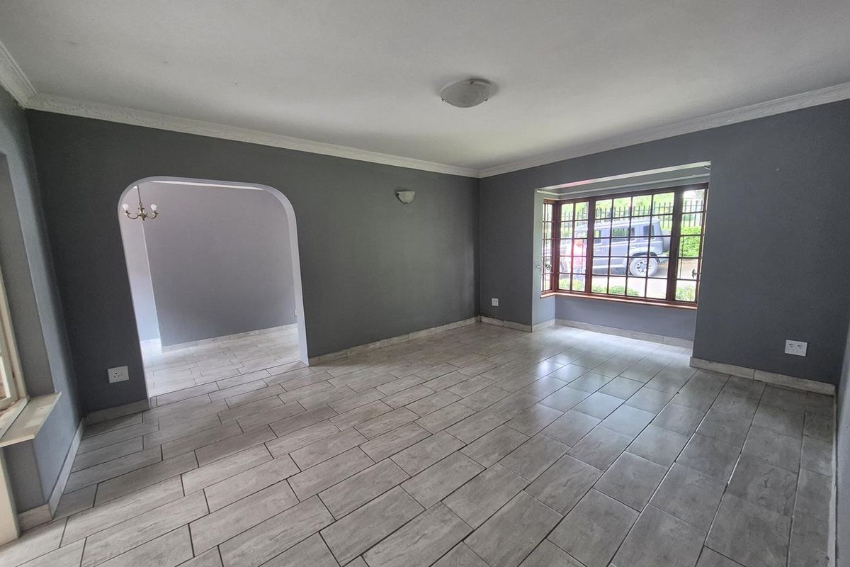 A spacious, empty living room featuring neutral grey walls, modern tiled flooring, and a large bay window that allows for ample natural light.