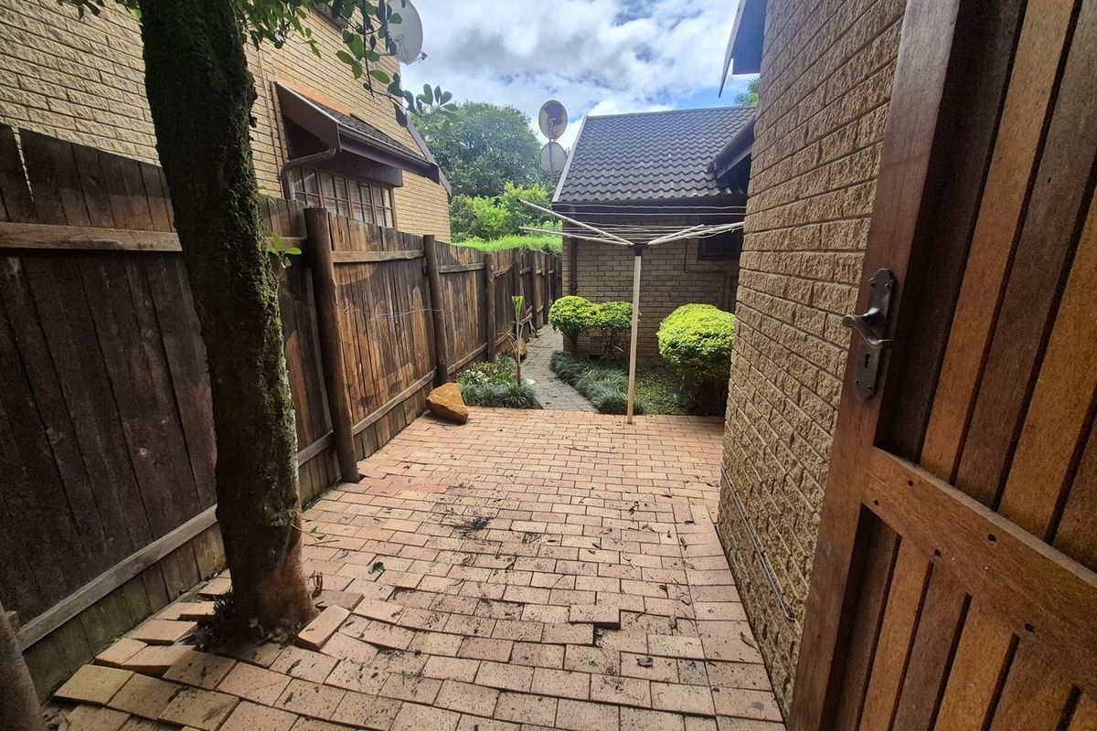 A rear exterior view of the townhouse featuring a brick-paved courtyard, timber fencing, and a rotary clothesline set against the building facade.