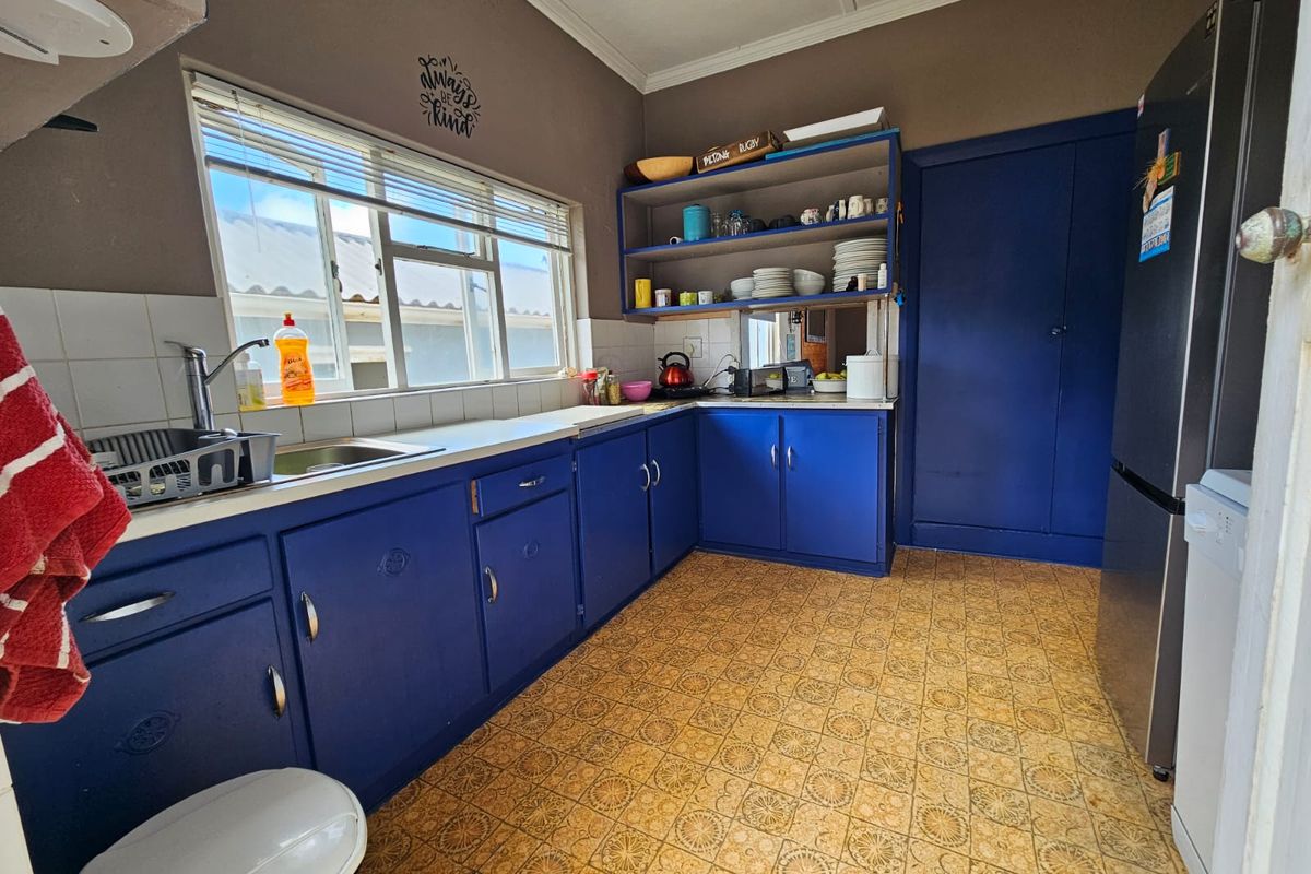 A functional kitchen featuring blue cabinetry, laminate countertops, a stainless steel sink, and vintage-style patterned vinyl flooring.