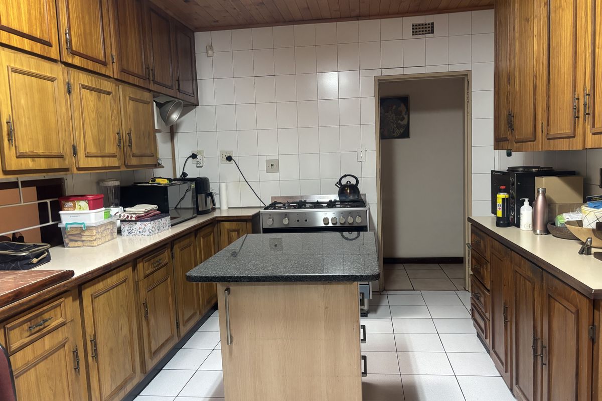 A functional kitchen featuring wooden cabinetry, granite countertops, a central island, and a gas stove with a tiled backsplash and flooring.